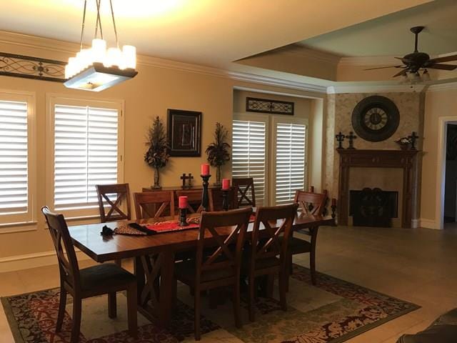 dining space featuring ornamental molding, ceiling fan with notable chandelier, a fireplace, and a tray ceiling