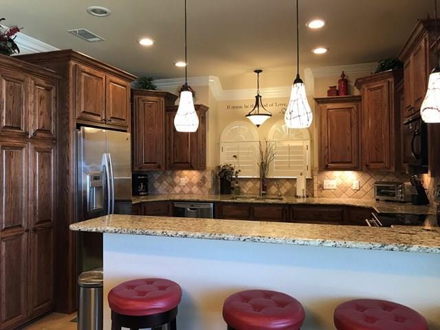 kitchen featuring a breakfast bar, decorative light fixtures, sink, decorative backsplash, and light stone countertops