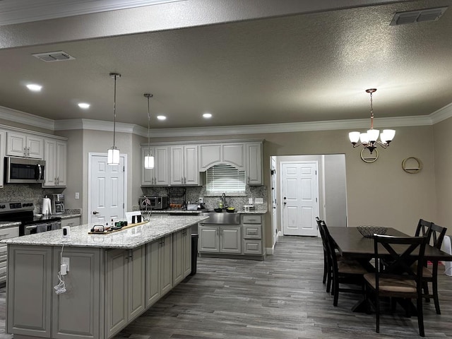 kitchen with appliances with stainless steel finishes, backsplash, gray cabinetry, a notable chandelier, and an island with sink