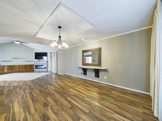 unfurnished living room featuring vaulted ceiling, hardwood / wood-style flooring, a fireplace, ceiling fan with notable chandelier, and ornamental molding