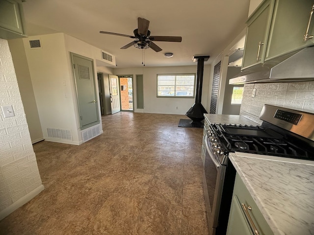 kitchen with visible vents, green cabinets, decorative backsplash, a wood stove, and stainless steel gas range