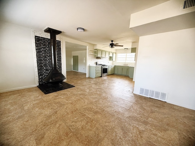 unfurnished living room with a wood stove, a ceiling fan, visible vents, and a sink