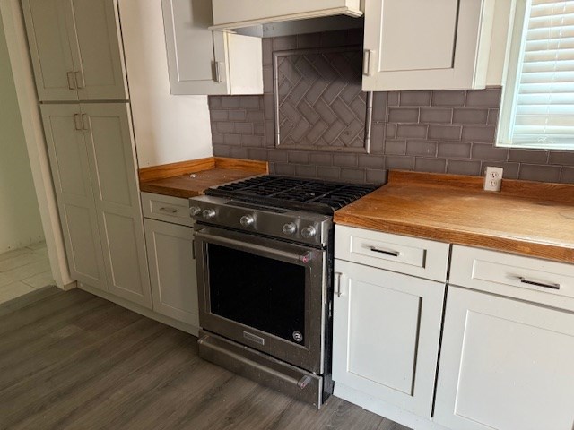 kitchen with white cabinets, decorative backsplash, dark wood-style floors, high end stainless steel range oven, and premium range hood