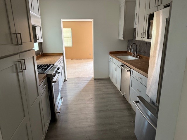 kitchen with dark wood-style flooring, tasteful backsplash, dark countertops, appliances with stainless steel finishes, and a sink