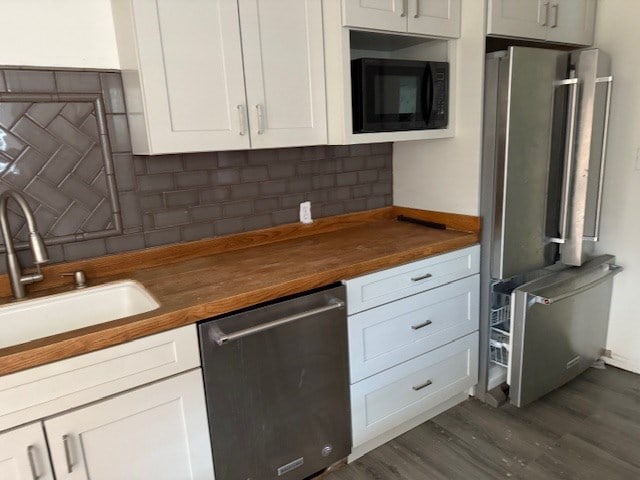 kitchen with white cabinets, butcher block counters, backsplash, stainless steel appliances, and a sink