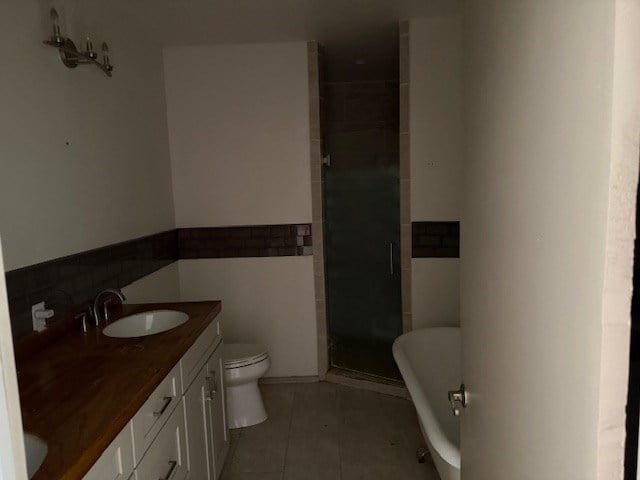 bathroom featuring double vanity, toilet, a sink, a shower stall, and tile patterned floors