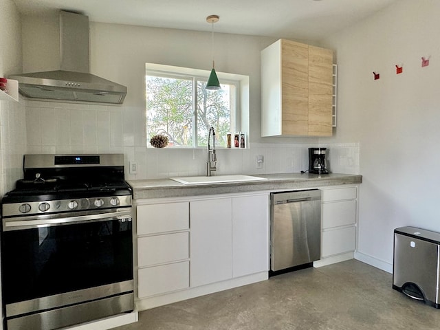 kitchen with white cabinets, wall chimney range hood, hanging light fixtures, sink, and appliances with stainless steel finishes