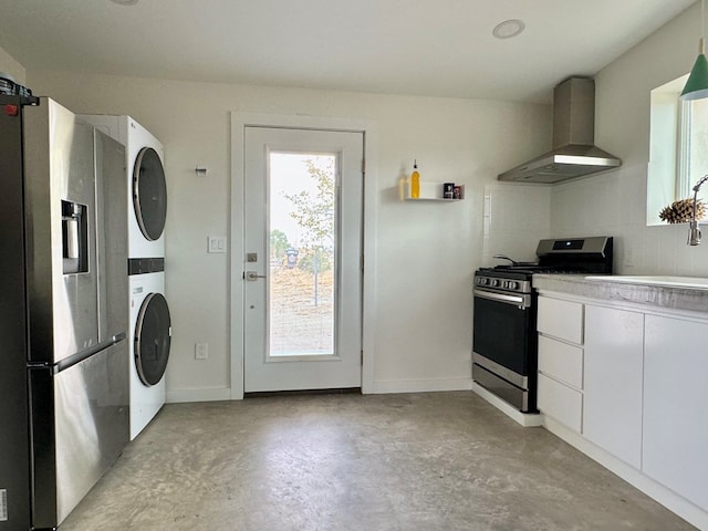 kitchen featuring sink, wall chimney exhaust hood, white cabinetry, stacked washer / dryer, and stainless steel appliances