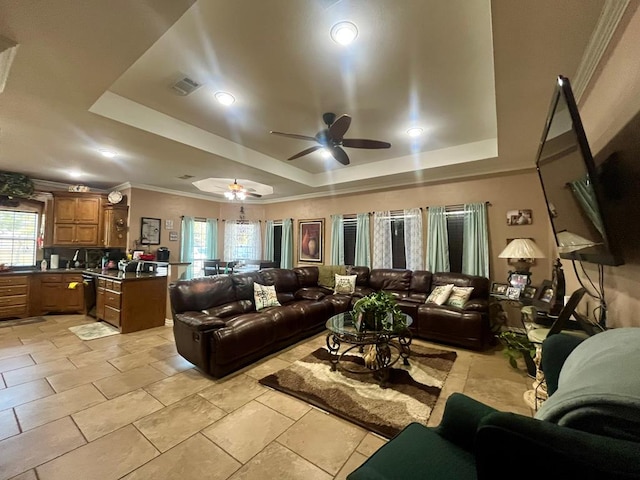 living room with a raised ceiling, ceiling fan, and ornamental molding