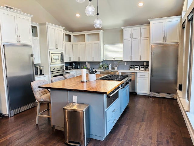 kitchen with decorative light fixtures, built in appliances, a center island, vaulted ceiling, and white cabinets