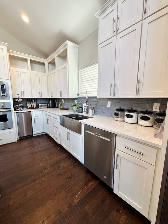 kitchen with stainless steel appliances, lofted ceiling, white cabinets, and backsplash