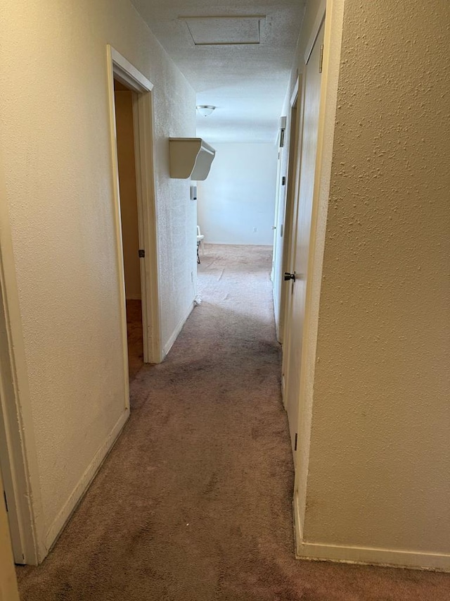 hallway with a textured wall, carpet floors, attic access, and baseboards