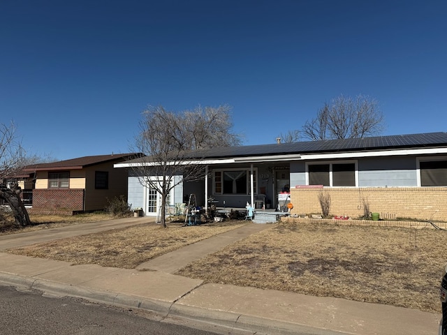 single story home featuring a garage, concrete driveway, solar panels, a porch, and brick siding