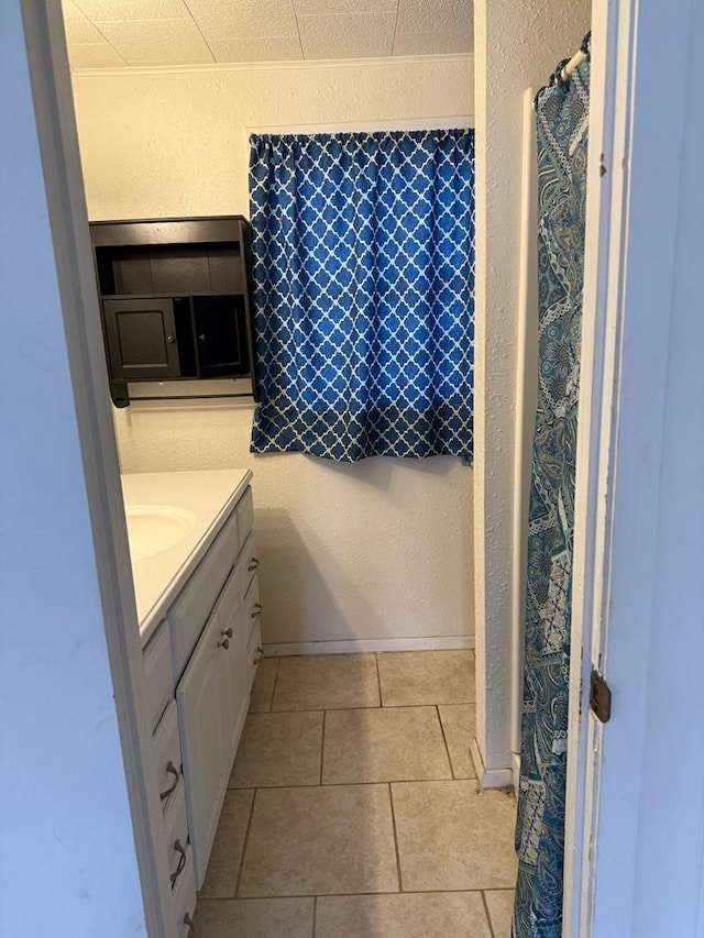 bathroom with a textured wall, tile patterned flooring, vanity, and baseboards