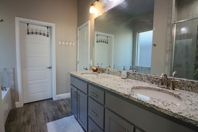 bathroom with a shower stall, wood finished floors, double vanity, and a sink