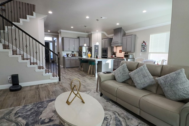 living area with recessed lighting, crown molding, light wood finished floors, baseboards, and stairs