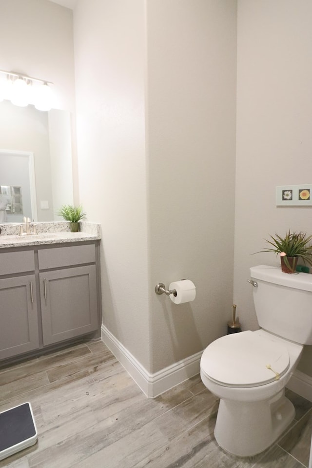 half bathroom featuring toilet, vanity, baseboards, and wood finished floors