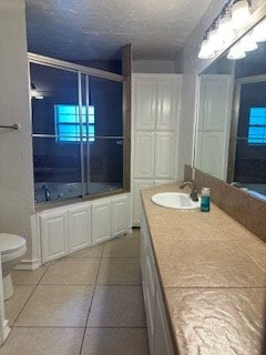 full bathroom with bath / shower combo with glass door, a textured ceiling, vanity, tile patterned flooring, and toilet