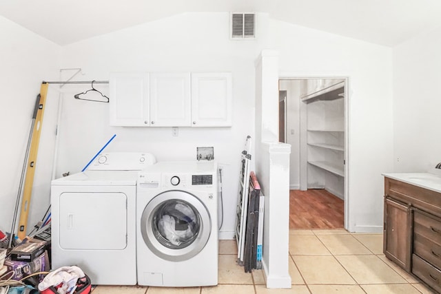 clothes washing area with washing machine and clothes dryer, sink, light tile patterned flooring, and cabinets