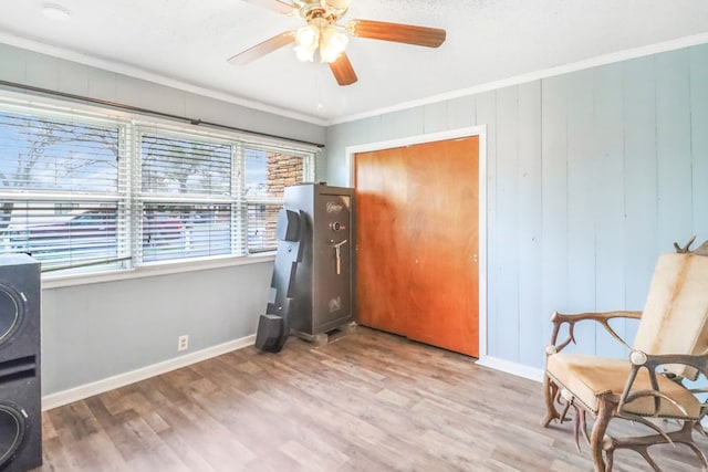 living area with crown molding, wooden walls, ceiling fan, and light wood-type flooring