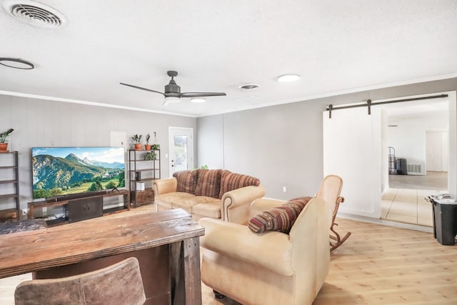 living room with a barn door, light hardwood / wood-style floors, ceiling fan, and ornamental molding