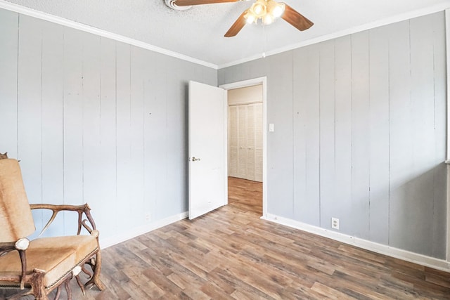 unfurnished room featuring hardwood / wood-style flooring, ceiling fan, crown molding, and wooden walls