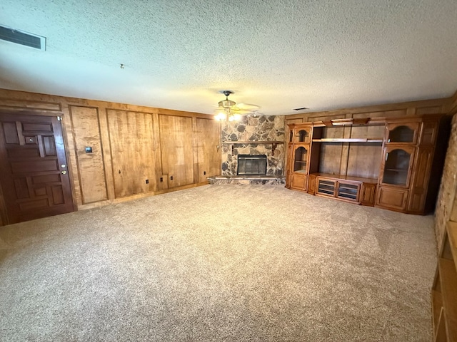 unfurnished living room featuring carpet, a textured ceiling, a fireplace, and wood walls