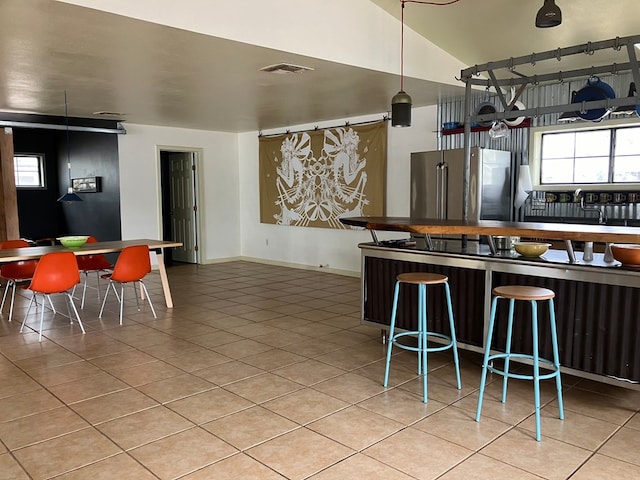 kitchen featuring a breakfast bar, stainless steel fridge, light tile patterned floors, and vaulted ceiling