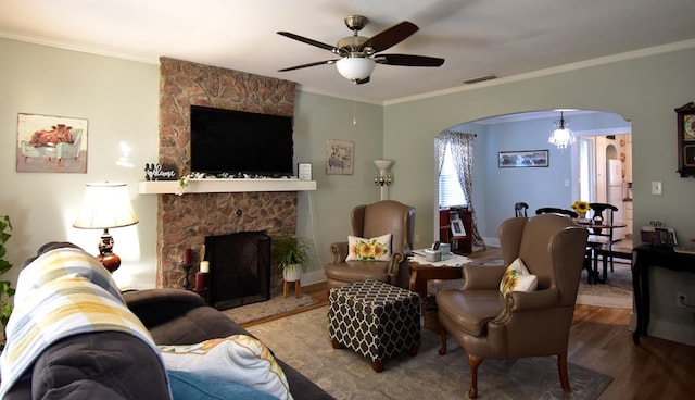 living room featuring a fireplace, wood-type flooring, ceiling fan with notable chandelier, and crown molding