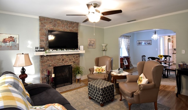 living room with a stone fireplace, hardwood / wood-style floors, ceiling fan with notable chandelier, and ornamental molding