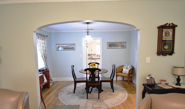 dining space with light wood-type flooring, crown molding, and a notable chandelier