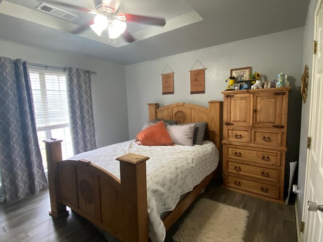 bedroom with ceiling fan, dark hardwood / wood-style floors, and a tray ceiling