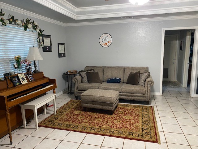 living room featuring a tray ceiling, ornamental molding, and light tile patterned flooring