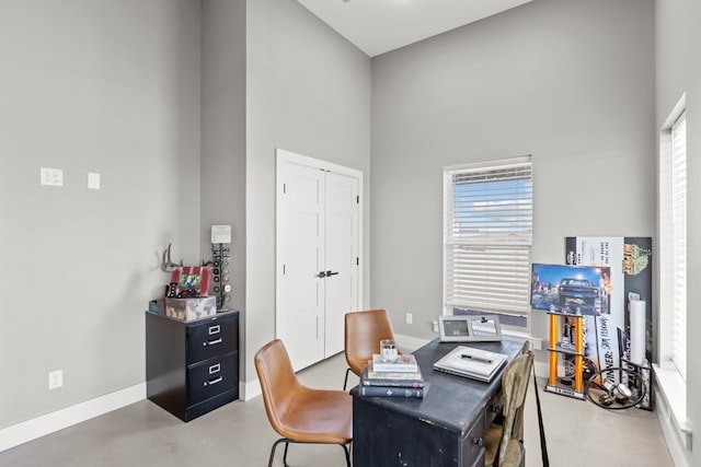 home office featuring a towering ceiling and concrete flooring