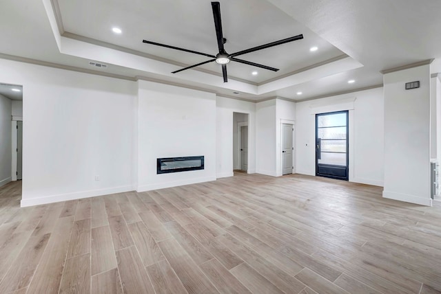 unfurnished living room with light wood-type flooring, a tray ceiling, visible vents, and a glass covered fireplace