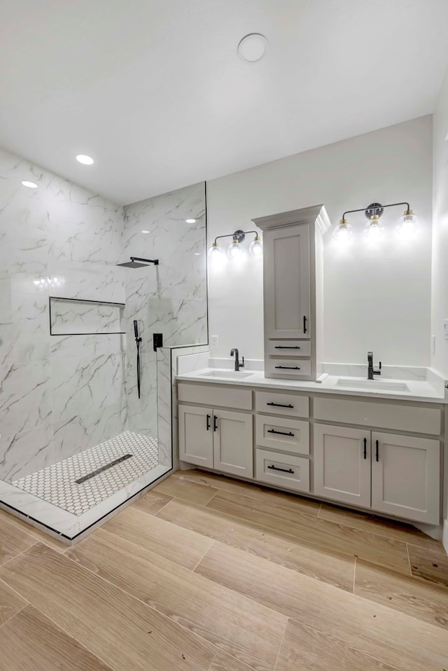 full bathroom with a marble finish shower, double vanity, wood tiled floor, and a sink