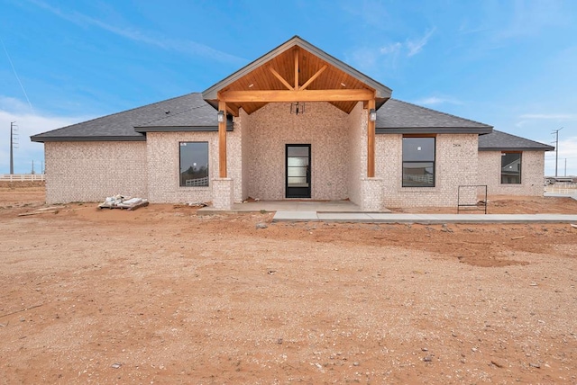 rear view of property with a patio, brick siding, and a shingled roof