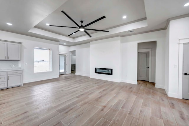 unfurnished living room featuring light wood-style flooring, a raised ceiling, and a glass covered fireplace