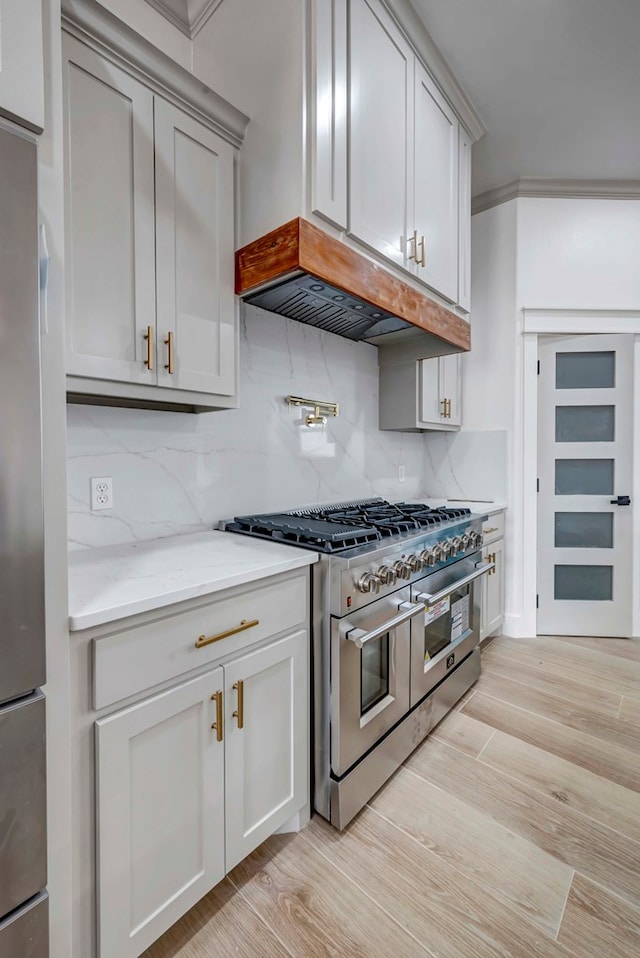 kitchen with backsplash, ventilation hood, light stone countertops, light wood-style floors, and stainless steel appliances