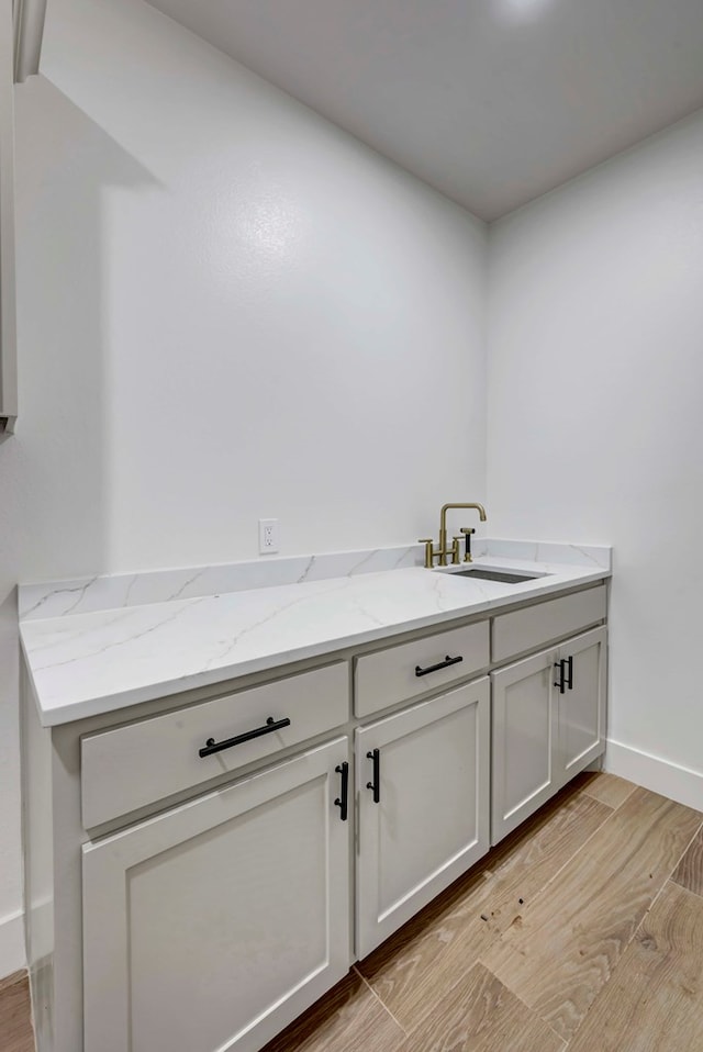 interior space with light stone countertops, baseboards, light wood finished floors, and a sink