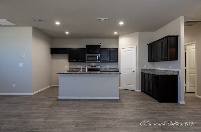 kitchen with sink, stone countertops, a center island with sink, dark hardwood / wood-style flooring, and stainless steel appliances