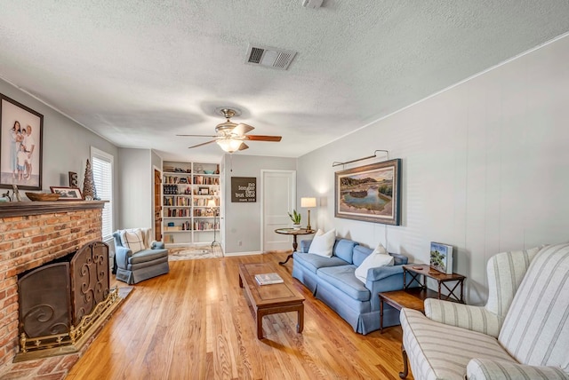 living area with a textured ceiling, visible vents, built in features, light wood-style floors, and a brick fireplace