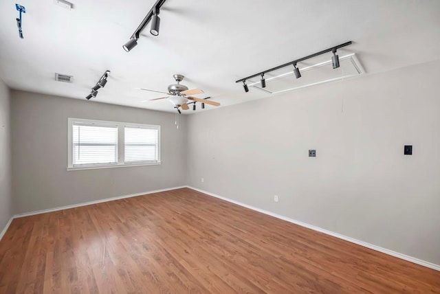 spare room featuring wood finished floors, visible vents, baseboards, attic access, and track lighting