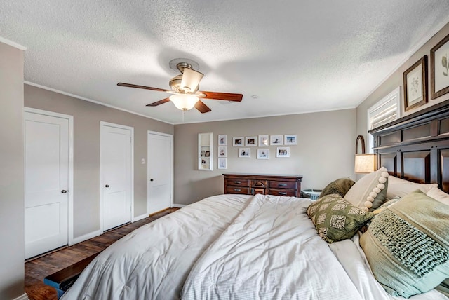 bedroom with baseboards, ceiling fan, ornamental molding, dark wood-type flooring, and multiple closets