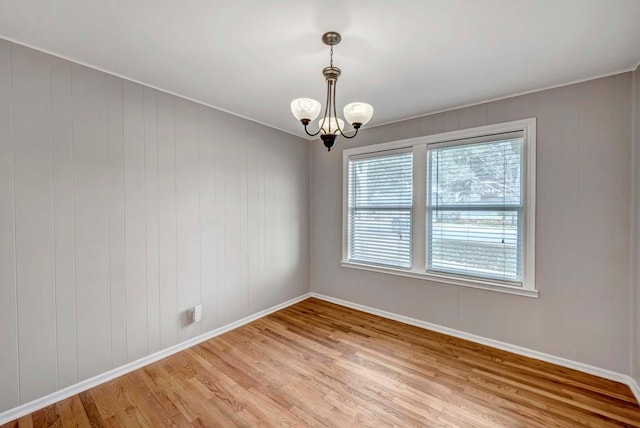 unfurnished room featuring baseboards, wood finished floors, and a notable chandelier