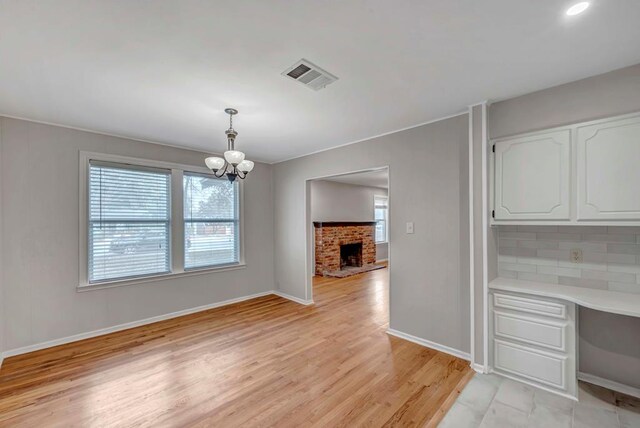 unfurnished dining area with light wood finished floors, baseboards, visible vents, a fireplace, and a notable chandelier