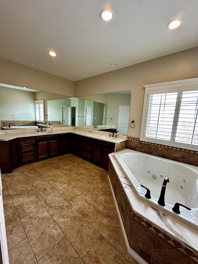 full bathroom with double vanity, a jetted tub, and recessed lighting