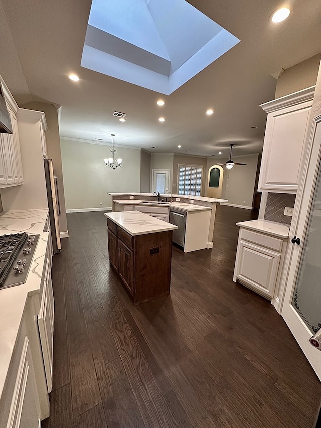 kitchen with dark wood-style floors, a kitchen island with sink, a sink, appliances with stainless steel finishes, and white cabinetry