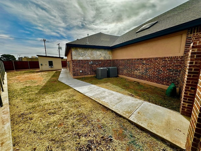 view of property exterior with an outbuilding, fence, a yard, central AC, and brick siding