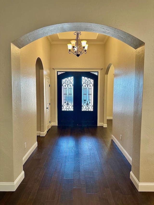 foyer entrance featuring hardwood / wood-style floors, a notable chandelier, a textured wall, and arched walkways